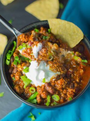 A bowl of chili topped with sour cream, green onions, and tortilla chips