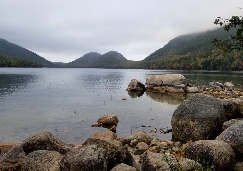 A view of Jordan Pond in Acadia National park with a rocky shoreline and mountains in the background