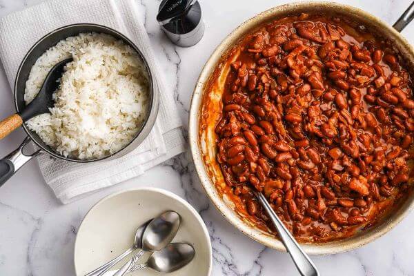 A pan with cooked red beans and a bowl of white rice on the side