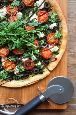 A cutting board with a Spinach and Goat's Cheese Arugula Tart on it.  Pizza cutter is placed on the side.