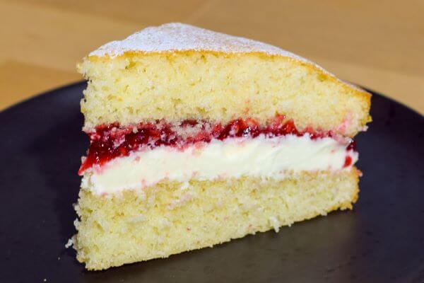 A slice of a Victoria Sponge Cake on a black plate